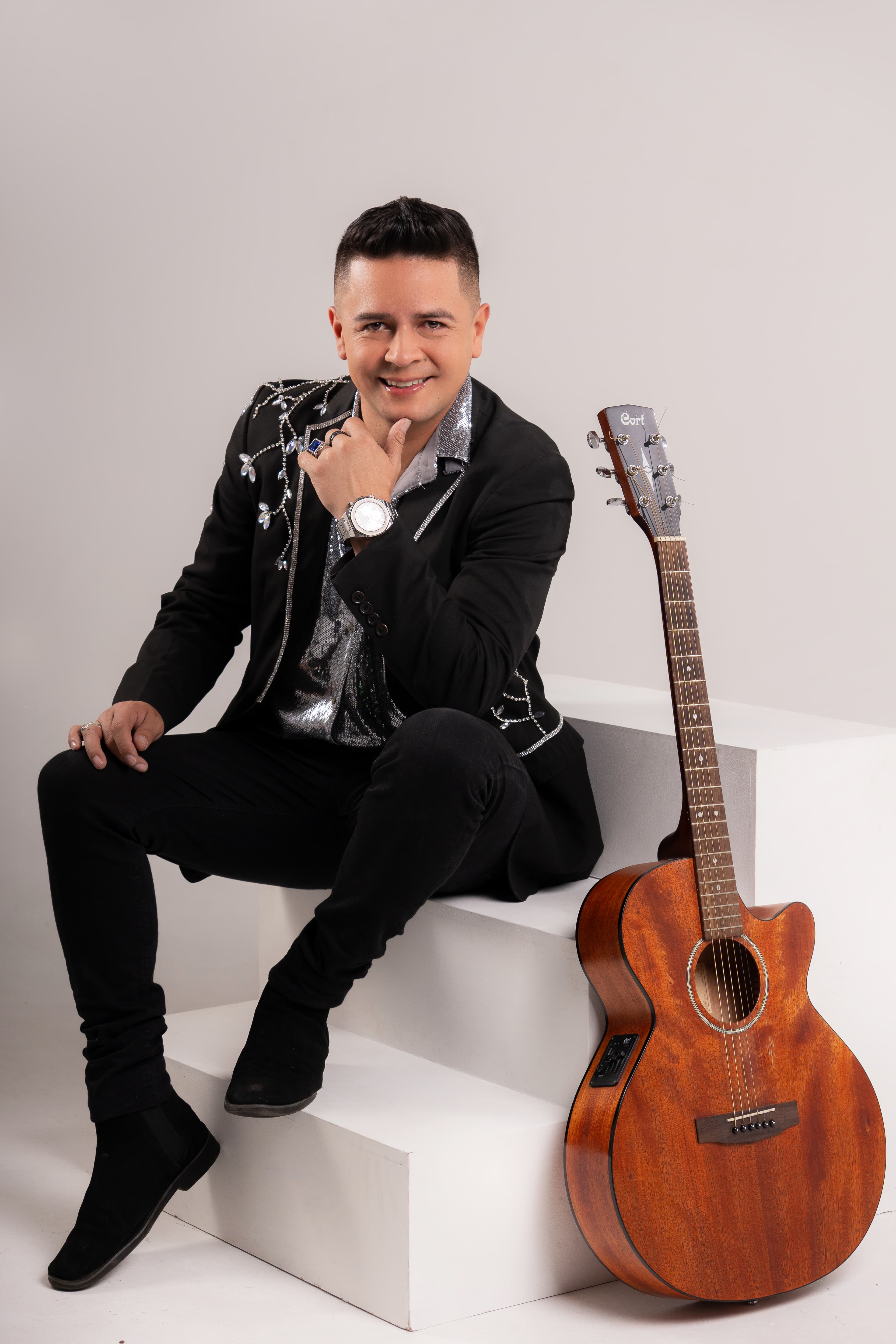 Mao Martínez sentado junto a una guitarra en una sesión editorial de estudio